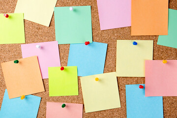 Cork board with a lot of pinned colored blank notes.