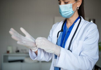 Portrait of woman doctor putting on gloves in hospital, coronavirus concept.