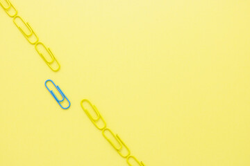 Design to blue clip separated alone from yellow clips on yellow paper background. This creative shows the different ideas or paradoxical, and unique. different idea concept.