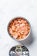 Open tin can of tuna fish, top view, white marble background, copy space. Canned food concept.
