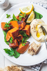 Close up of baked sweet potato slices with spinach and hummus on white plate. Plant based food concept.