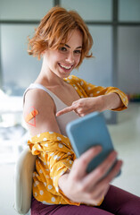 Happy woman with plaster on arm after vaccination in hospital, taking selfie.