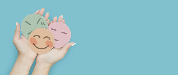 Woman hand holding emotion group of paper cut happy smile face, angry and boring face on blue background, positive and negative thinking, mental health assessment , world mental health day concept
