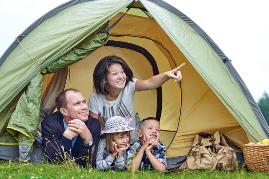 Family Parents And Two Children In Camp Tent. Happy Mother, Father, Son And Daughter On Summer Vacation. Mom Showing Something In Distance