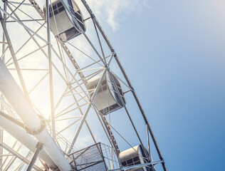 Gray or white metal ferris wheel with closed passenger cabins close-up in the amusement park