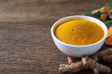  Turmeric powder in a white bowl and fresh turmeric (curcumin) on wooden background,Used for...