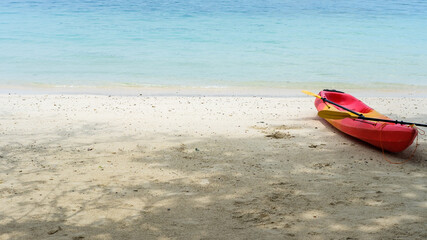 red canoe on the sandy beach with shade of the trees, blue sea and sky background.