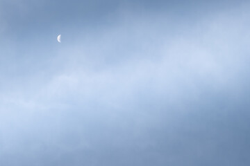 Half-moon during the day, cloudy blue sky.