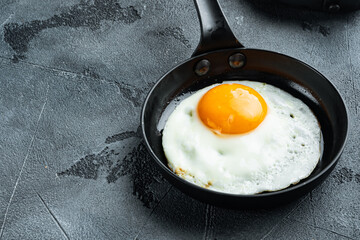 Fried eggs with cherry tomatoe and bread for breakfast in cast iron frying pan, on gray background , with space for text  copyspace