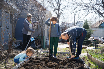 multi generational family work together in the garden and open the beds with a shovel near the house. slow life. enjoy the little things. 