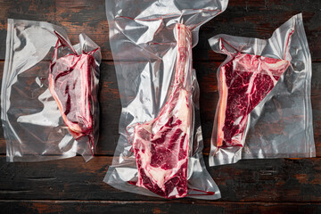 Raw beef dry aged steak vacuum sealed bag for sell, tomahawk, t bone and club steak cuts, on old dark  wooden table background, top view flat lay