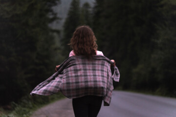Journey. Adventure. a girl in a plaid shirt is walking along the road around the forest.
