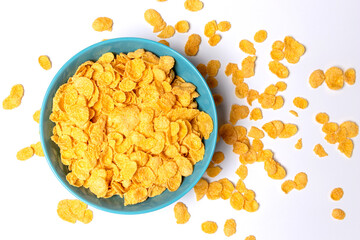 Cornflakes in a blue cup isolated on a light background. Scattered cornflakes lie nearby. Top view.