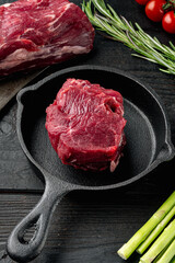 Beef fillet cut raw with ingredients, in cast iron frying pan, on black wooden table background