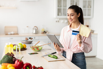 Woman shopping online using tablet and credit card in kitchen