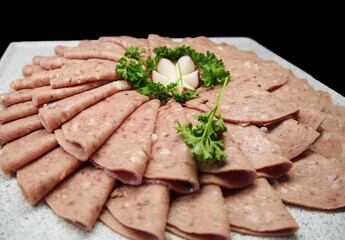 Folded ham slices artistically arranged on a tray, with vegetables on top