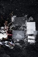 On the black ground lie wedding rings, gray and white cards, a bouquet of flowers, ribbon and colored pencils. The postcard depicts a white church on a black background