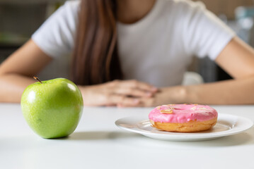 Obraz na płótnie Canvas Woman on dieting for good health concept. Close up female comparing favourite donut and green apple for good health.