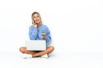 Young blonde Uruguayan girl with the laptop isolated on white background holding coffee to take away and a mobile