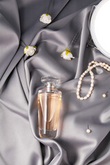 Glass bottle of aromatic luxury floral perfume on grey background of fabric drapery. Still life of perfume, mirror, beads, earrings and hairpins