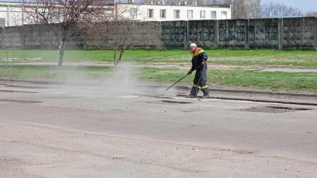 Worker blows out the pieces of old asphalt and stones from the pits by leaf blower on the road. Cleaning and blowing water and debris from a surface during construction, road repair. Road construction