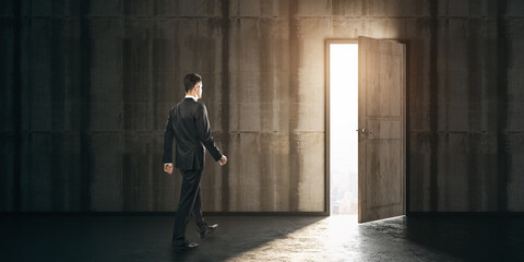Businessman walking towards exit in a dark concrete room. Leadership and future concept