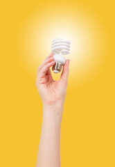 Female hand holding a LED light bulb on yellow background. Using economical and environmentally friendly light bulb concept. Idea. Energy saving lamp in woman's hand