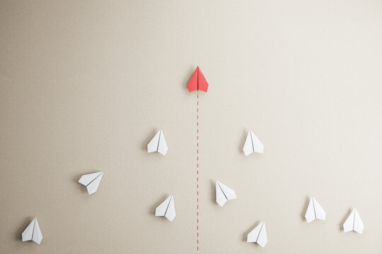 Success goal and creative idea concept with red paper plane compete with white paper planes on abstract beige wallpaper