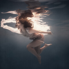 A girl with long dark hair swims underwater on a dark background as if floating in weightlessness