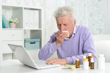 Fototapeta premium Portrait of sad sick senior man using laptop