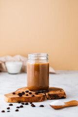 Iced coffee on wooden board with coffee beans. Cold summer drink with space for copy.