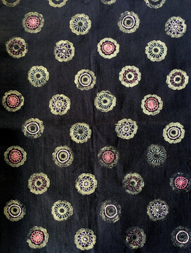 background close up of a black piece of textile with light yellow stencilled flowers decorated with embroidery