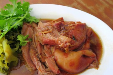 Stewed pork leg with coriander and pickled cabbage on white plate. Thai style food.