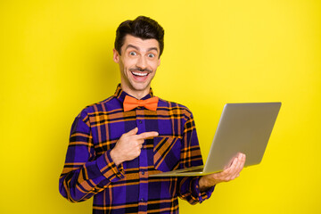 Photo of young excited man happy smile indicate finger laptop ad recommend advise isolated over yellow color background
