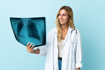 Young blonde Uruguayan doctor woman isolated on blue background looking to the side and smiling