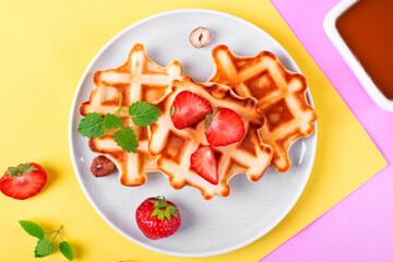  Waffles with strawberry and mint served on ceramic plate on geometric background. Top view