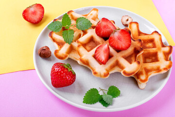  Waffles with strawberry and mint served on ceramic plate on geometric background. Top view