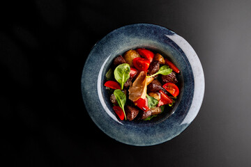 Salad with smoked beef and vegetables, sweet peppers and tomatoes on a gray plate on a black background.