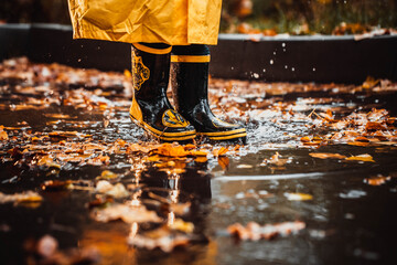 the child jumps into a puddle. legs in yellow rubber boots.