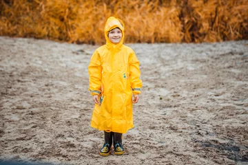 Fototapeten Boy in yellow raincoat on a deserted beach on a cloudy day © popovatetiana