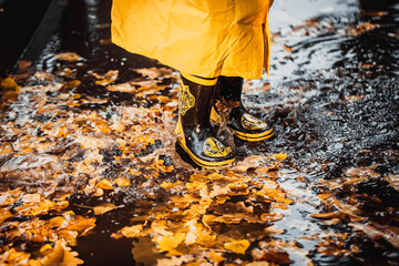 the child jumps into a puddle. legs in yellow rubber boots.