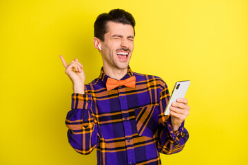 Photo of young handsome crazy excited man listen music in earphones hold cellphone isolated on yellow color background