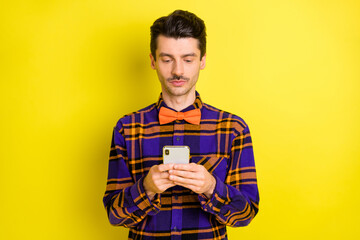 Photo of young serious man look browse internet cellphone chat type sms isolated over yellow color background