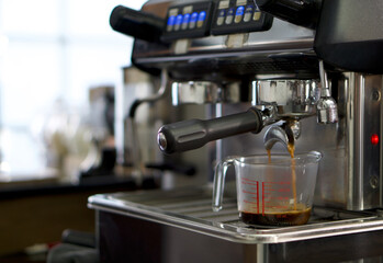 Espresso machine pouring coffee in measuring cup. Close up