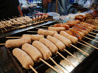 Sausages and other meats on skewers grilling in an open stove at a street market