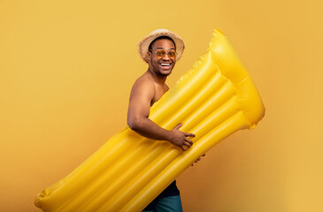 Swimming is fun. Joyful black man in swimwear going to pool with inflatable lilo over yellow studio...
