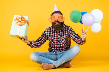 funny brutal bearded man wear checkered shirt having lush beard and moustache hold party balloons and present box, birthday