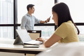 Obraz premium Businessman using cell phone with woman working on laptop in foreground.