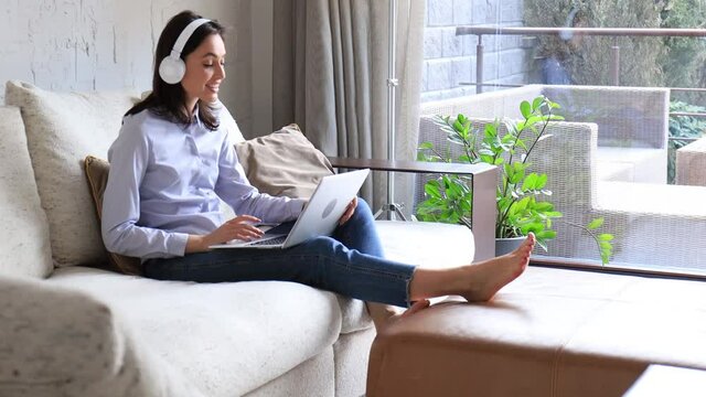 Young attractive smiling caucasian woman using laptop sitting on sofa at home, singing song, enjoying free time. Girl student studying design apps on digital touchpad.