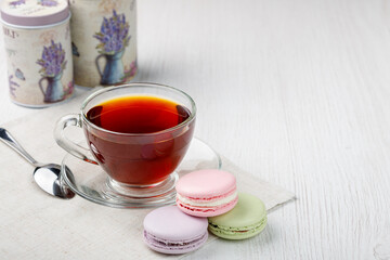 Multicolored macaroons and a cup of tea on a light wood kitchen table. Morning tea and sweets.